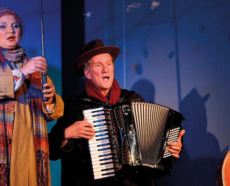 Zwei Darsteller:innen auf der Bühne des Nachmittagstheaters in der Kulturhalle Süßen – eine singt, der andere spielt Akkordeon. Bunte Kleidung und Bühnenlicht erzeugen eine warme Atmosphäre.