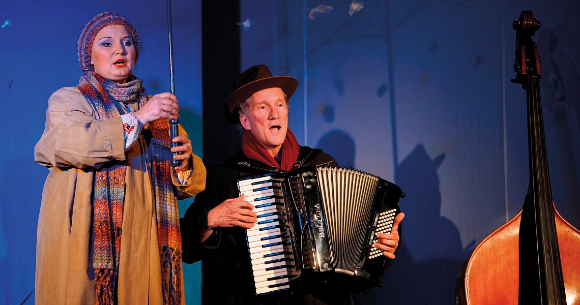 Zwei Darsteller:innen auf der Bühne des Nachmittagstheaters in der Kulturhalle Süßen – eine singt, der andere spielt Akkordeon. Bunte Kleidung und Bühnenlicht erzeugen eine warme Atmosphäre.