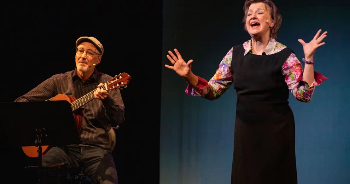 Dolce Vita zwischen Wunder und Wahnsinn Szene aus dem Programm „Bella Italia“ in der Kulturhalle Süßen: Eine Künstlerin singt und erzählt mit lebhafter Gestik, begleitet von einem Gitarristen auf der Bühne.