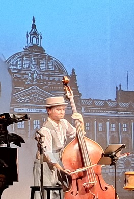 Musiker im Retro-Outfit spielt Kontrabass vor projizierter Berliner Kulisse der 1920er Jahre.