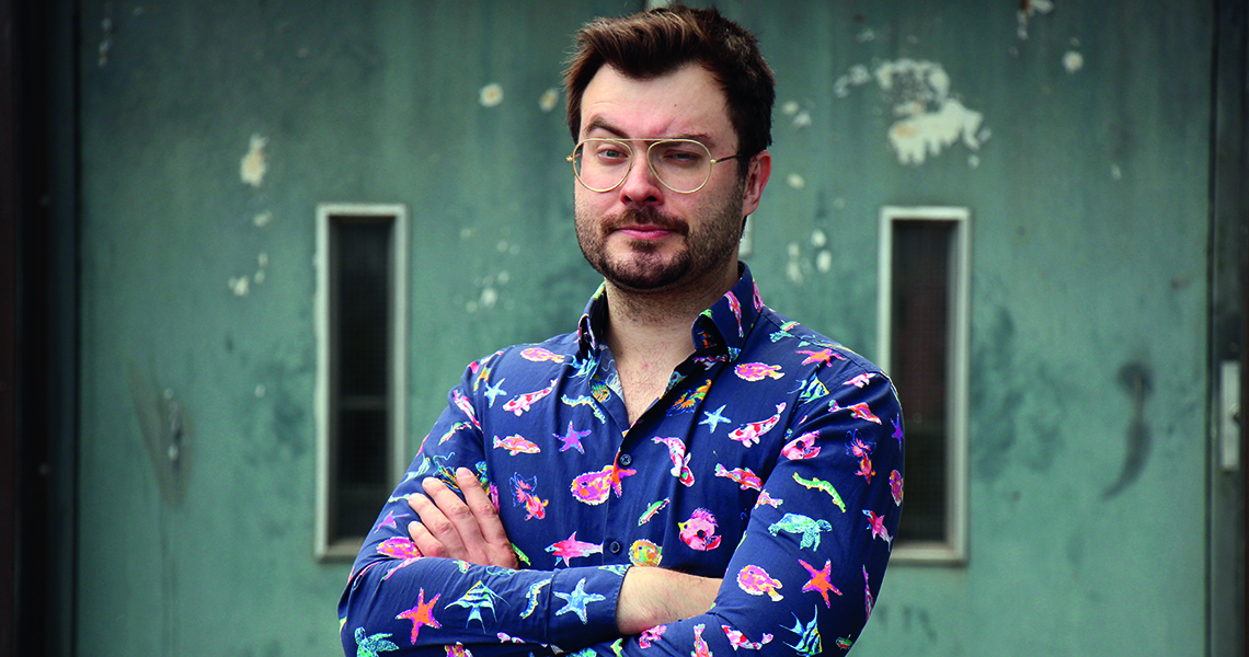 Der Quiz-Master Sebastian Klussmann in der Kulturhalle Süßen Bild von Sebastian Klussmann, der die Arme verschränkt und ein Auge zukneift.