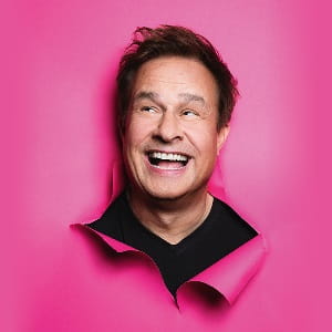 Lars Reichow Lachender Mann vor kräftig pinkfarbenem Hintergrund, moderner Porträtstil mit dynamischer Wirkung.