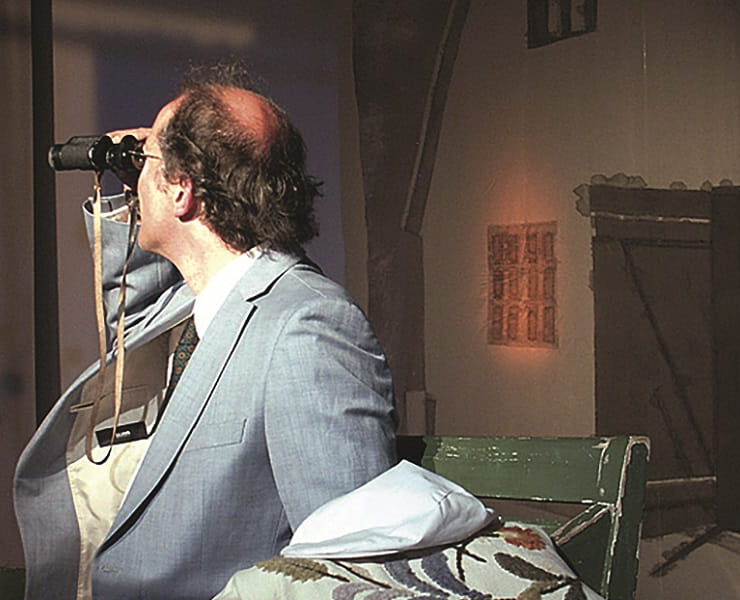 Ein Mann sitzt auf einer Bühne und blickt durch ein Fernglas in die Ferne. Nachmittagstheater: Dositza, bloß so dositza