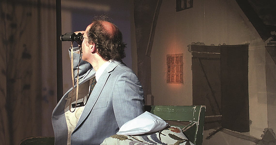 Nachmittagstheater: Dositza, bloß so dositza Ein Mann sitzt auf einer Bühne und blickt durch ein Fernglas in die Ferne. Nachmittagstheater: Dositza, bloß so dositza
