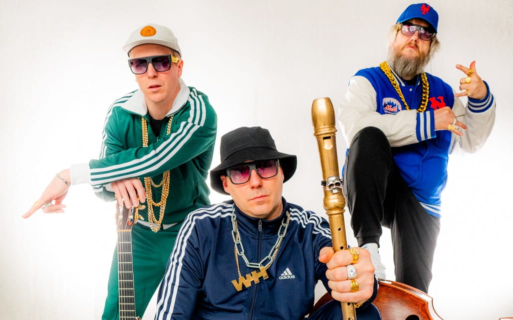 Wildes Holz in der Kulturhalle Süßen Pressefoto von Wildes Holz zum Programm „Block-Party“: Die drei Musiker posieren in Trainingsjacken, Sonnenbrillen und mit Goldketten vor hellem Hintergrund. Einer hält eine Blockflöte in die Kamera.
