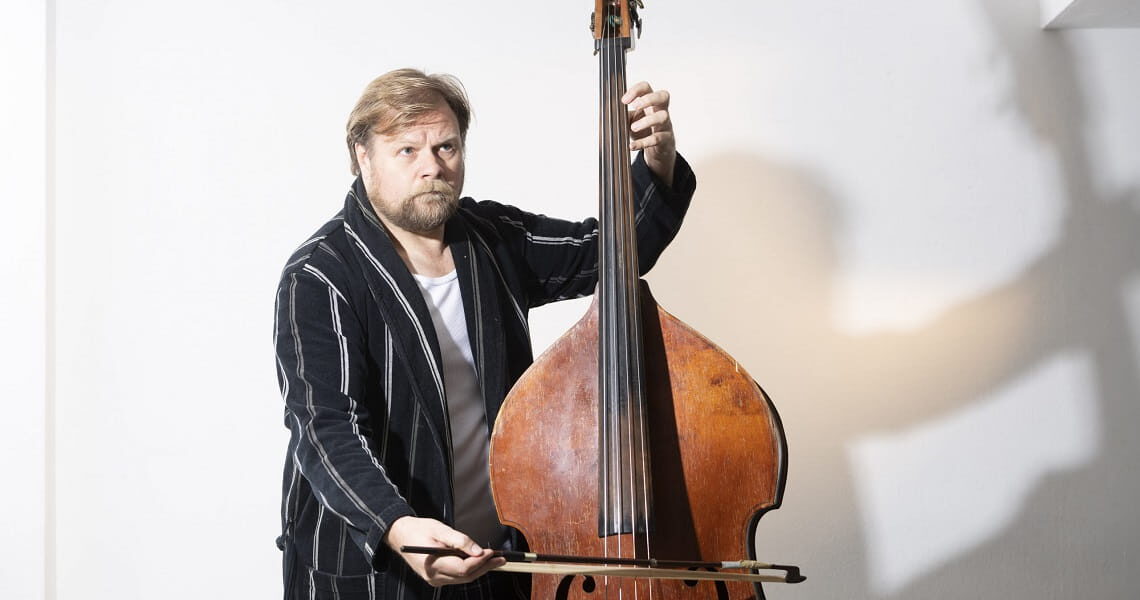 Michael A. Grimm posiert mit Kontrabass und Bogen vor hellem Hintergrund – passend zum Theaterstück „Der Kontrabass“ von Patrick Süskind.
