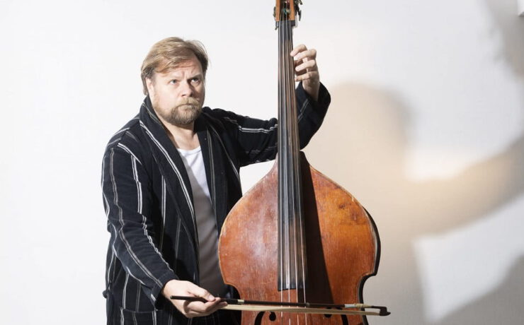 Michael A. Grimm posiert mit Kontrabass und Bogen vor hellem Hintergrund – passend zum Theaterstück „Der Kontrabass“ von Patrick Süskind.