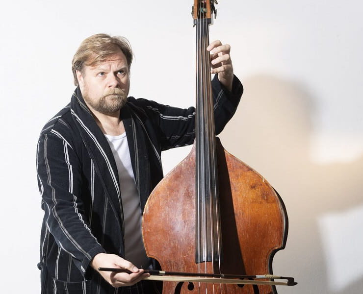 Michael A. Grimm posiert mit Kontrabass und Bogen vor hellem Hintergrund – passend zum Theaterstück „Der Kontrabass“ von Patrick Süskind.
