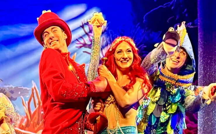Szene aus dem Familienmusical „Die kleine Meerjungfrau“ mit farbenfrohen Kostümen, Unterwasser-Bühnenbild und Figuren wie Meerjungfrau, Krabbe und Fisch.