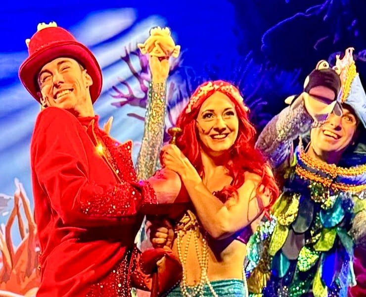 Szene aus dem Familienmusical „Die kleine Meerjungfrau“ mit farbenfrohen Kostümen, Unterwasser-Bühnenbild und Figuren wie Meerjungfrau, Krabbe und Fisch.