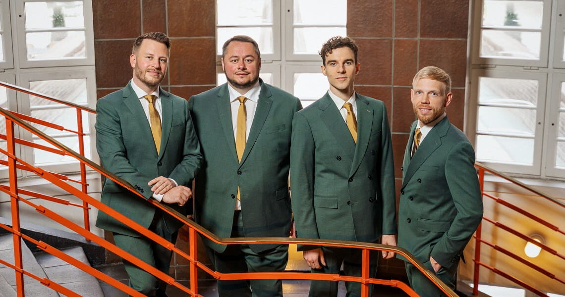 Die vier Sänger von Quartonal posieren in grünen Anzügen auf einer Treppe mit rotem Geländer – passend zum Silvesterkonzert „Songbook – tierisch gut ins neue Jahr“.