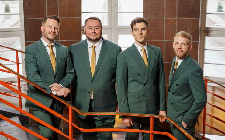Die vier Sänger von Quartonal posieren in grünen Anzügen auf einer Treppe mit rotem Geländer – passend zum Silvesterkonzert „Songbook – tierisch gut ins neue Jahr“.