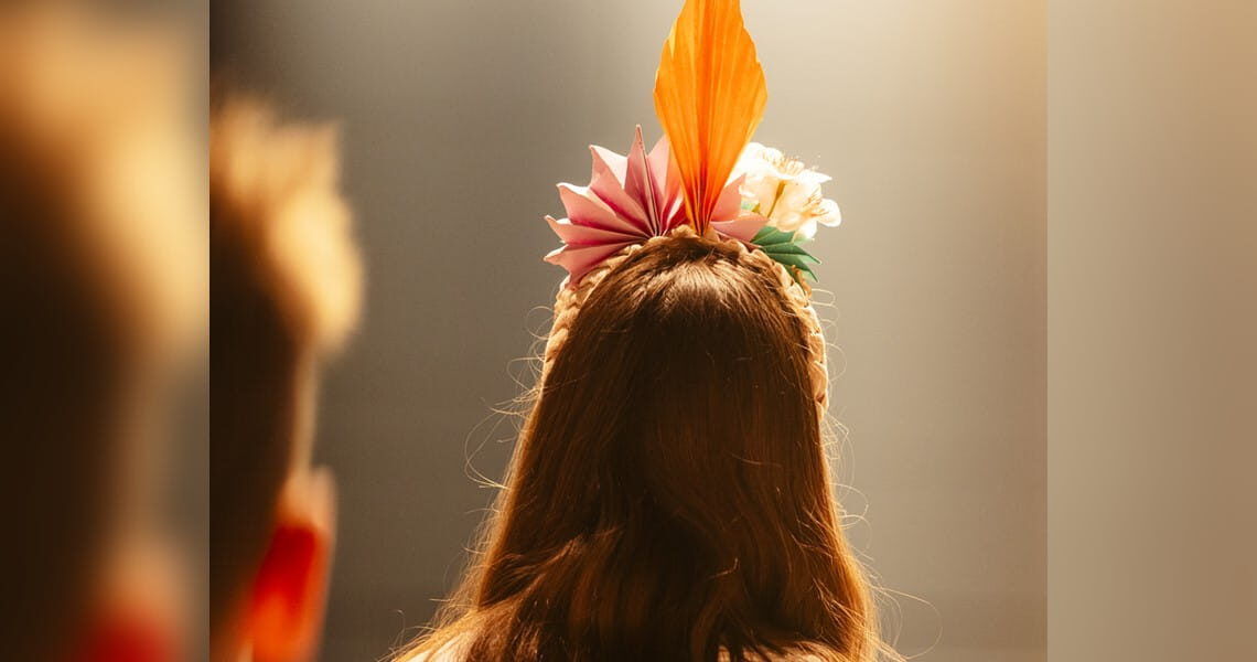 Blick von hinten auf eine Person mit farbenfrohem Kopfschmuck im warmen Bühnenlicht – passend zum Stadtfestkonzert der Kolping-Musikschule Süßen.