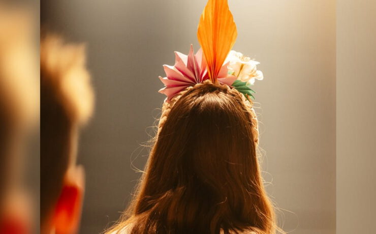 Blick von hinten auf eine Person mit farbenfrohem Kopfschmuck im warmen Bühnenlicht – passend zum Stadtfestkonzert der Kolping-Musikschule Süßen.