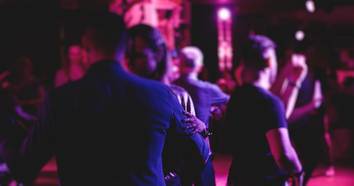 Tanzende Gäste feiern bei stimmungsvoller violett-pinker Beleuchtung auf einer Tanzfläche – passend zur Veranstaltung „Tanz in den Mai“ mit Live-Musik.