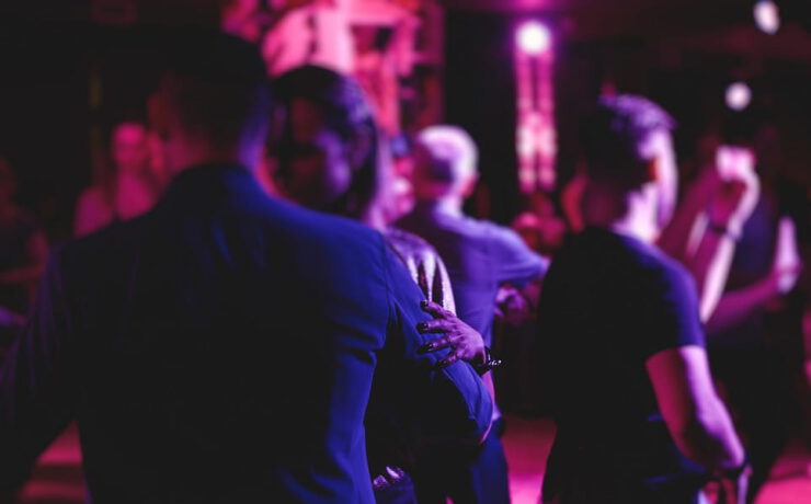 Tanzende Gäste feiern bei stimmungsvoller violett-pinker Beleuchtung auf einer Tanzfläche – passend zur Veranstaltung „Tanz in den Mai“ mit Live-Musik.