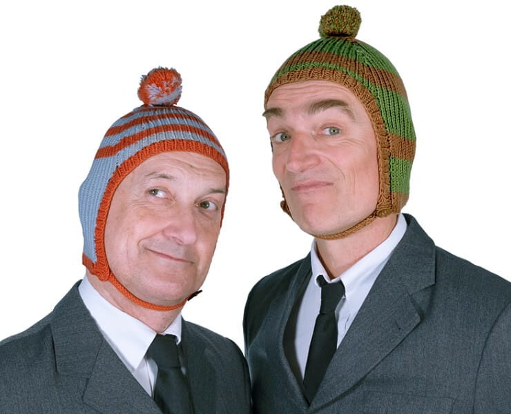 Die beiden Künstler von Ulan & Bator posieren in grauen Anzügen mit bunten Strickmützen und schauen verschmitzt in die Kamera.